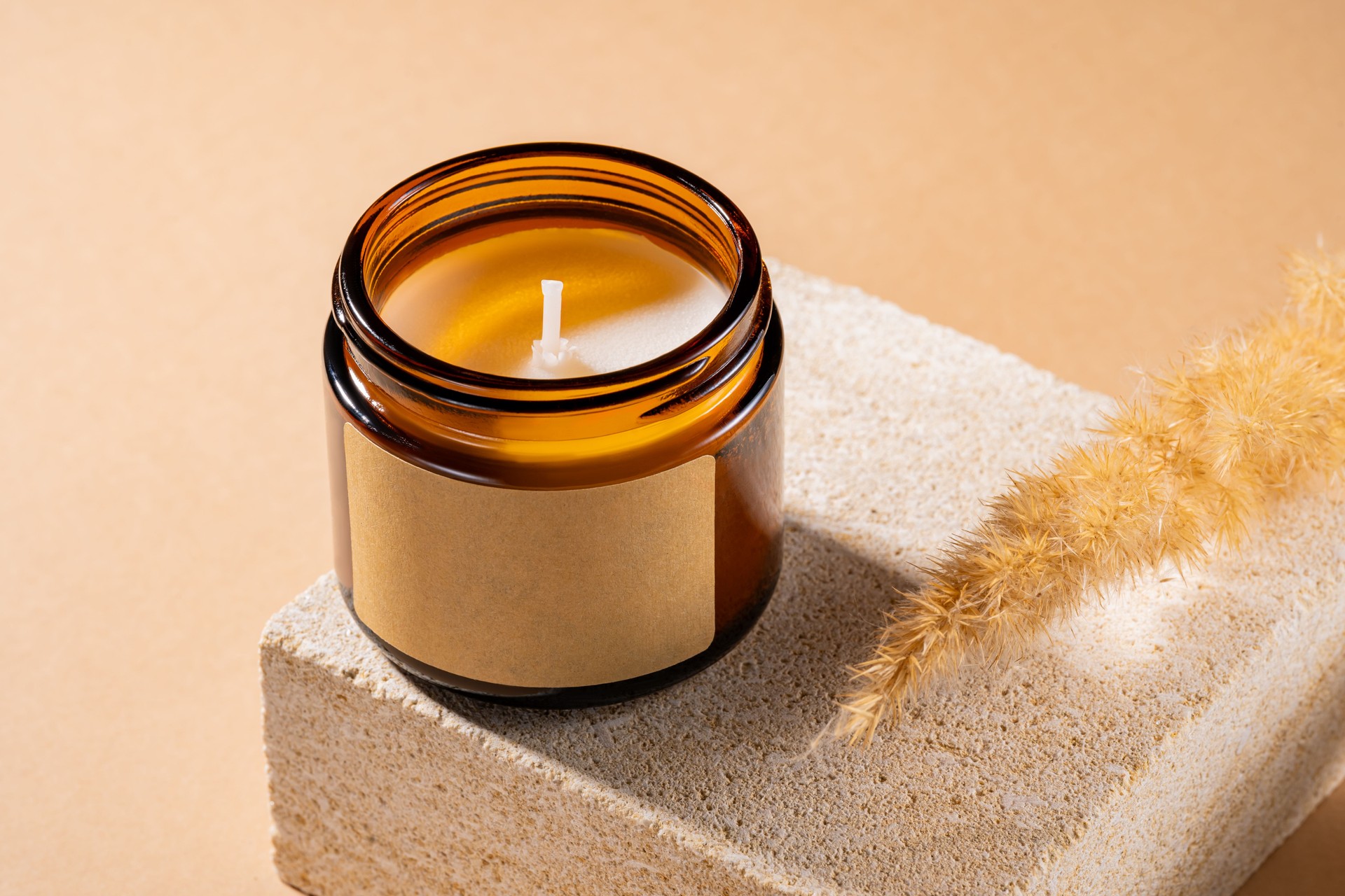 Mock-up of aroma soy candle in amber glass jar on natural stone pedestal. Scented cozy atmosphere for relax and spa on brown background, mockup